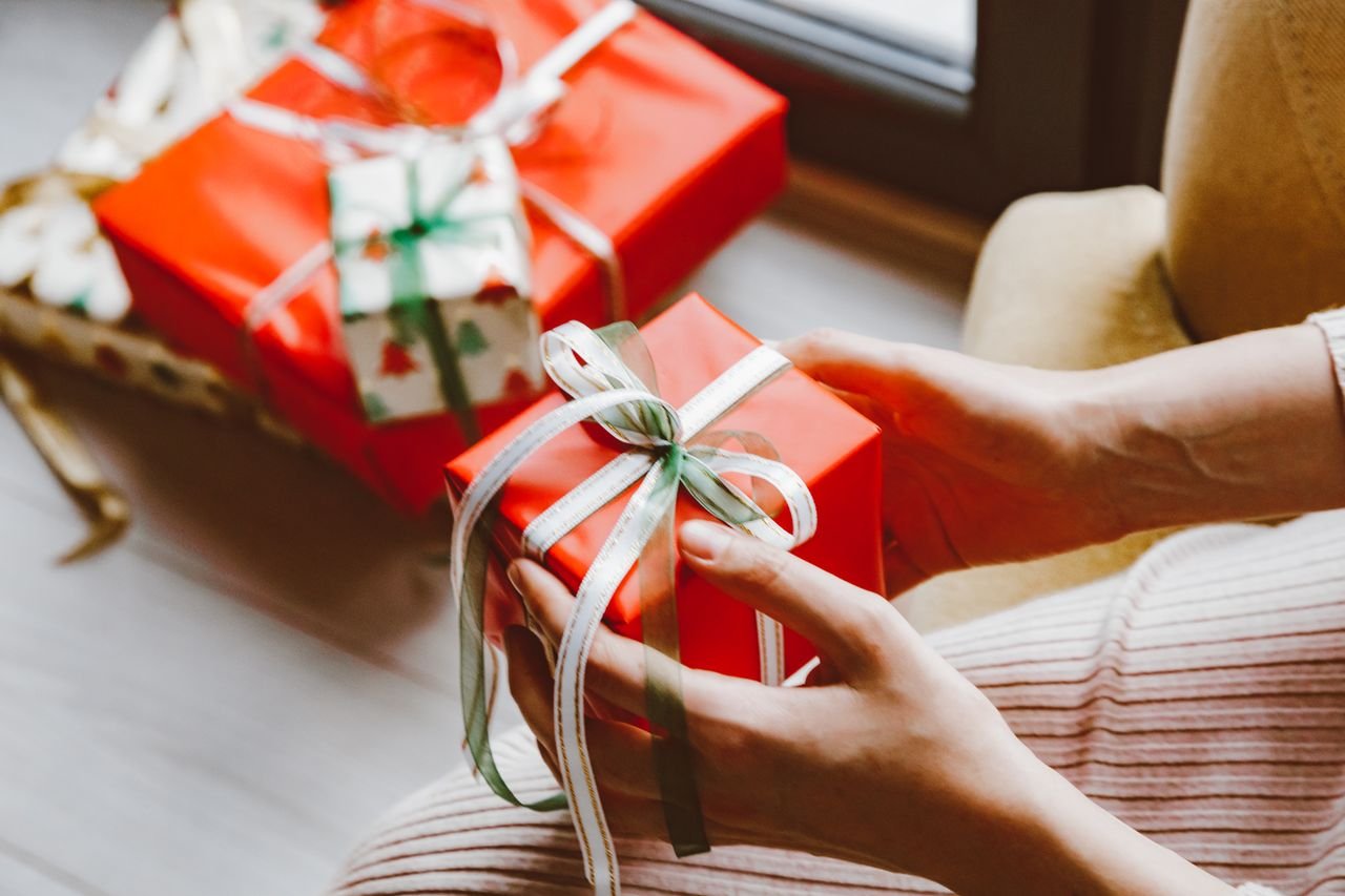 about-us Close-up of hands holding a wrapped Christmas gift tied with ribbon, capturing the festive mood.