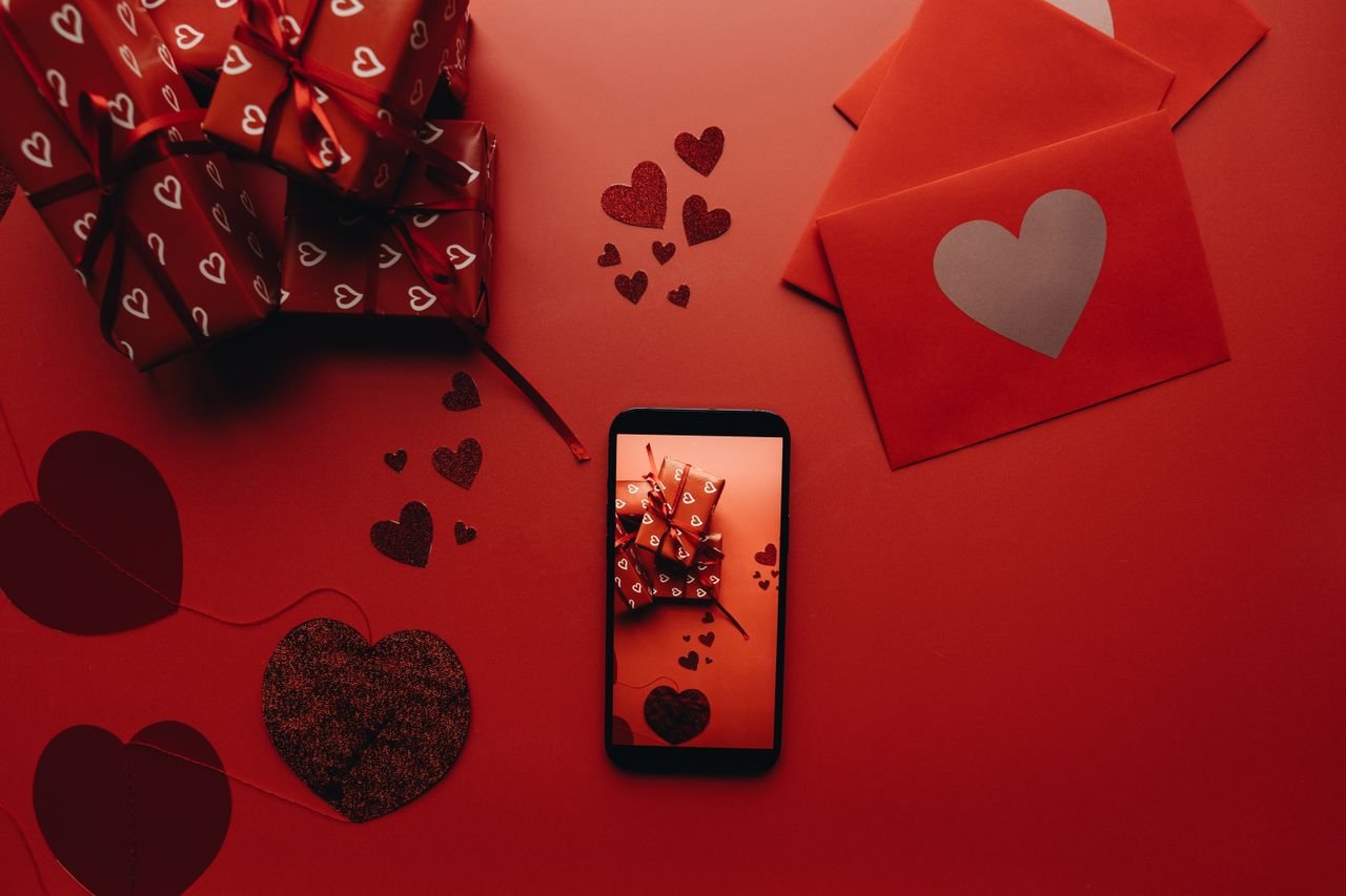 about-us Flat lay of Valentine's Day gifts, envelopes, and phone on a red background with heart motifs.