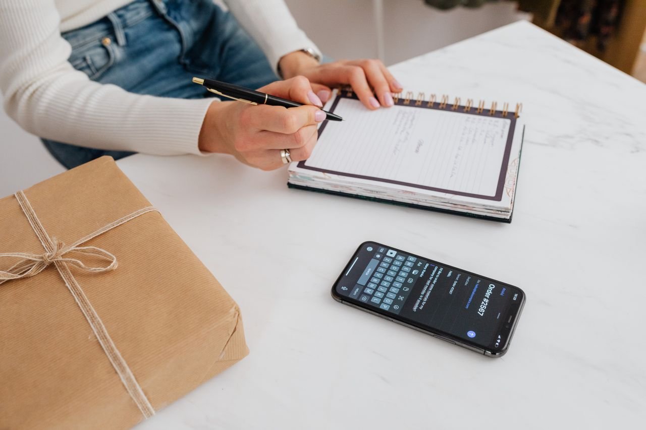 The Art of Drawing Readers In: Your attractive post title goes here Person writing in a notebook beside a smartphone on a marble table, emphasizing organization and planning.